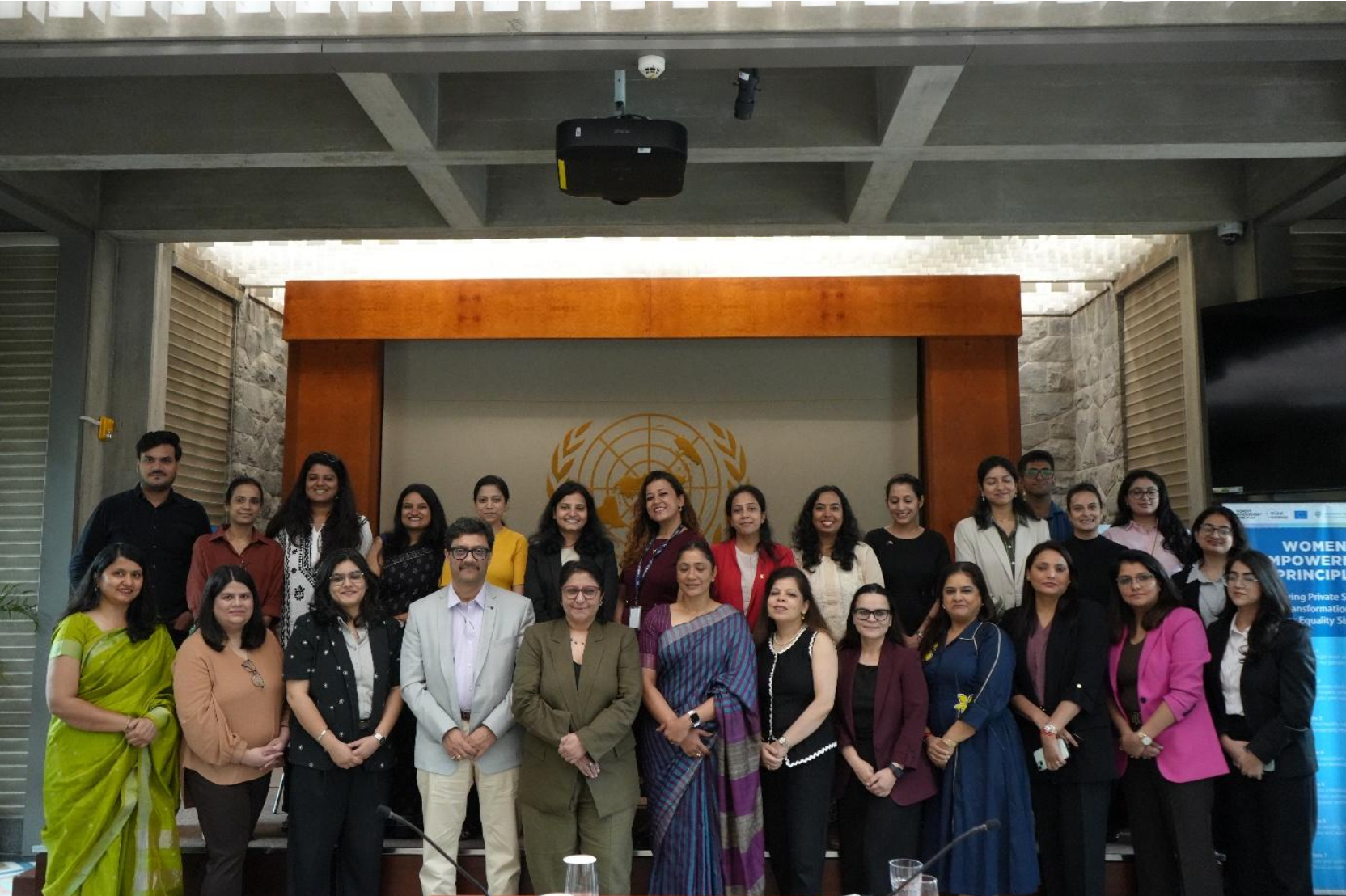 group of people posing for a photo indoors in front of the UN symbol